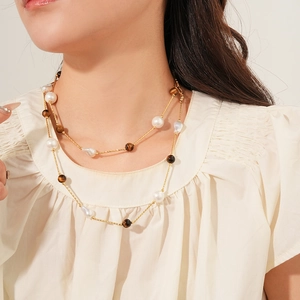 Close-up of double-layer necklace with gold chain, white pearls and tiger eye beads