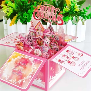3D pink Christmas pop-up card featuring a cozy snow house and snowman winter scene