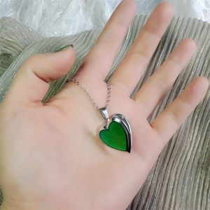 Detail of color-changing heart pendant necklace held on shimmering silver fabric