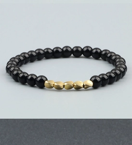 Detail of beaded bracelet featuring glossy black agate beads and twisted golden metal accents