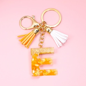 Detail of resin letter E keychain with embedded corn kernels, gold foil, and tassels