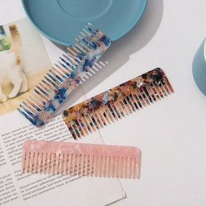 Three acetate hair combs with marble patterns and wide teeth on a stylish white desk