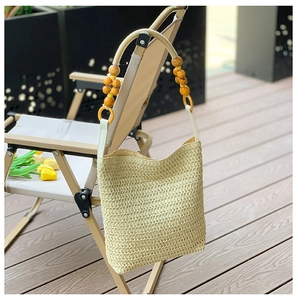 Detail of hand-woven beige straw bag featuring vibrant orange and yellow wooden bead handles