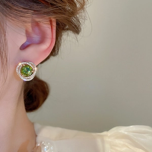 Macro view of gold flower earrings with green zircon center and pavé diamonds worn by model