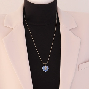 Detail of heart stone pendant with gold figure inlay on snake chain over beige blazer
