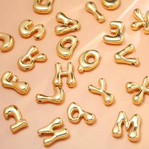 Macro shot of 18K gold-plated bubble alphabet beads on a soft pink surface