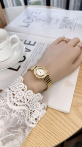 Close-up of a vintage gold flower-shaped watch on a woman's wrist with lace sleeve