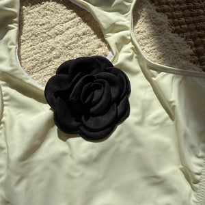 Detail of a large 3D black satin flower ornament on a cream-colored slim-fit swimsuit