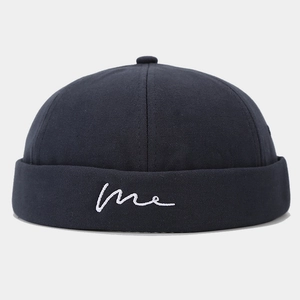 Detail of white cursive me embroidery on navy blue cotton dock worker cap brim