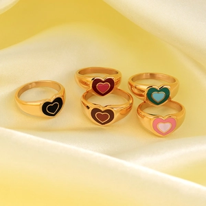 Five gold heart rings with colorful enamel filling on elegant yellow silk fabric background