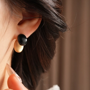 Close-up of gold and black oval stud earring worn on ear with soft focus background