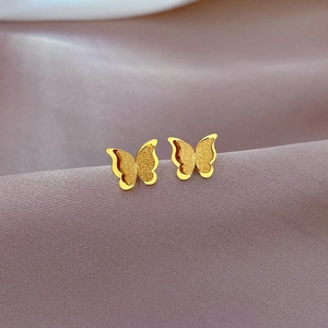 Macro detail of gold butterfly stud earrings with matte and polished finish on purple velvet
