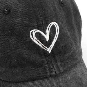 Close-up of white heart embroidery on a black washed cotton baseball cap texture