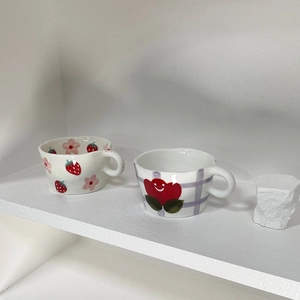 Detail of hand-painted ceramic mugs featuring strawberry and heart patterns on a shelf
