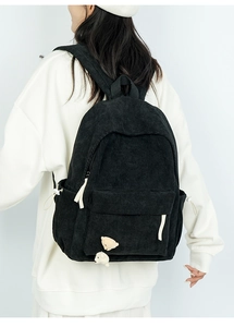 Detail eines schwarzen Cord-Rucksacks mit Bärenanhängern und vorderer Reißverschlusstasche