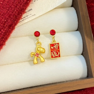 Macro detail of asymmetrical gold lion and red money tag earrings with pearl accents