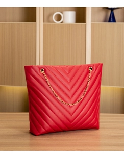 Detail of red PU leather tote with V-quilted pattern and gold chain strap on wood