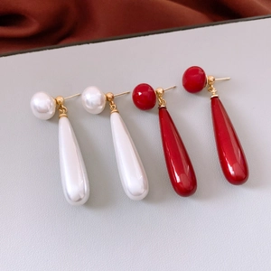 Detail of red and white teardrop pearl earrings with elegant gold metal accents