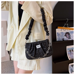Detail of black pleated shoulder bag with silver petal chain on a beige blazer