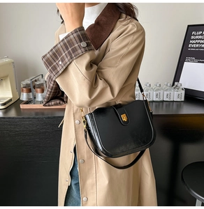 Close-up of black glossy saddle bag featuring gold metal buckle and adjustable strap