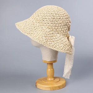 Beige straw sun hat with white lace bow on a wooden stand for summer vacation