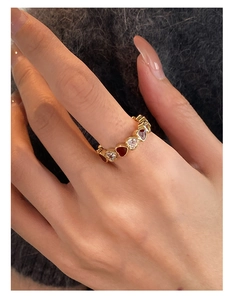 Close-up of gold-plated heart ring featuring red enamel and sparkling zircons on finger