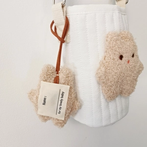 Detail of white quilted bottle bag with brown bear charm and leather name tag
