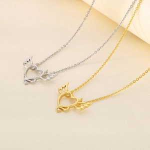 Detail of gold and silver heart necklaces with angel wings on a beige textured surface