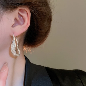 Macro view of a model wearing silver twisted textured S925 drop earrings with subtle shimmer