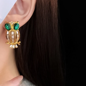 Detailed view of vintage gold owl earring with green gemstone eyes on model's ear