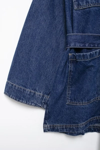 Detail of dark blue denim jacket featuring contrast gold stitching and utility pocket design