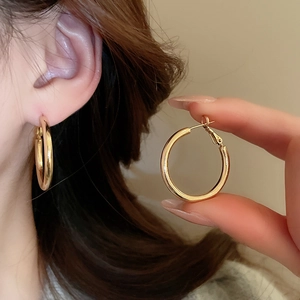 Detailed view of polished golden hoop earrings worn and held to show scale and texture