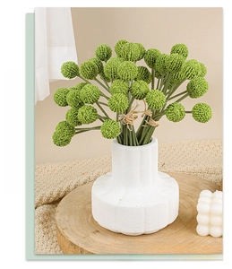 Artificial golden ball plants in a white ceramic vase on a rustic wooden tray