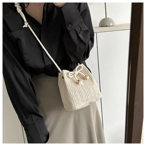 Detail of hand-woven straw bucket bag in off-white featuring a rope strap and drawstring