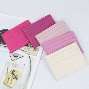 Detailed view of pink and beige lychee pattern leather card holders stacked on a magazine
