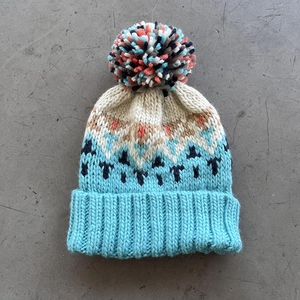 Close-up of winter knit beanie featuring geometric jacquard pattern and large pompom