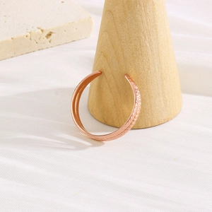 Detail of rose gold open cuff bracelet with hammered texture on a wooden stand