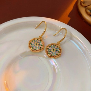 Macro detail of vintage gold floral enamel earrings on a glossy white display plate