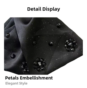 Macro shot of black satin fabric detail with beaded flower pattern and shimmering glitter