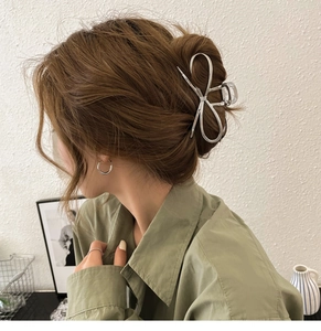 Silver bow hair claw clip shown on a model's updo hairstyle in a modern home setting