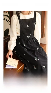 Detail of floral embroidery on a black cross-back linen apron with side pockets