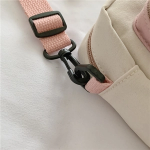 Detail of the pink woven strap and sturdy black clip on the white canvas bag