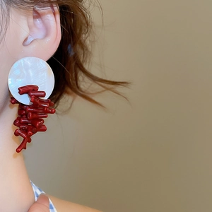 Close-up of model wearing large shell earrings with artistic red coral-like resin drops