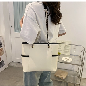 Detail of cream tote bag with black trim and elegant gold chain leather strap