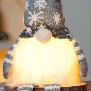 Detail of a glowing Christmas gnome with warm LED light, snowflake knit hat and wooden base