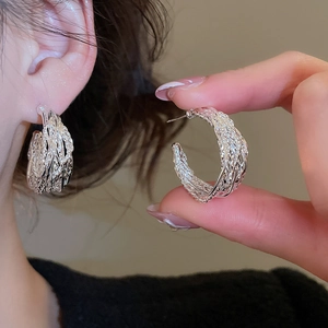 Macro detail of silver C-shaped twisted earrings featuring intricate woven metal texture