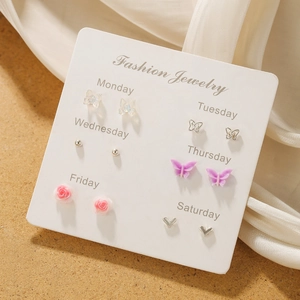 Detail view of 6-pair butterfly earring set on a wooden surface with weekly labels