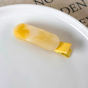 Close-up of yellow resin hair clip with gold glitter on white ceramic plate