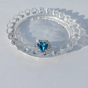 Macro shot of heart-cut blue sapphire ring with halo diamond setting on a glass tray