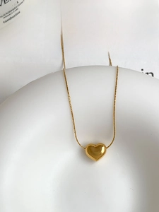 Close-up of a polished gold heart pendant necklace on a minimalist lifestyle background